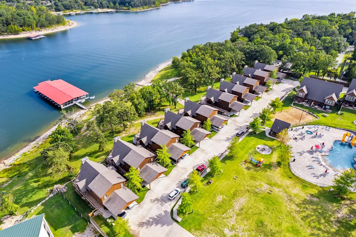 An inviting exterior shot displaying a row of family-friendly cabins situated alongside a sparkling lake, with a pool area and playground in view. The scene is lively and welcoming, with hints of outdoor recreation and relaxation opportunities for guests of all ages.