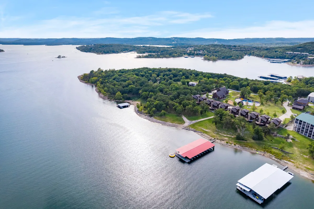 A sweeping view of the expansive lake, green island, and waterfront docks, with a cluster of cabins nestled along the shoreline. The tranquil setting is ideal for activities like boating, fishing, hiking, and picnicking, all surrounded by lush natural beauty.