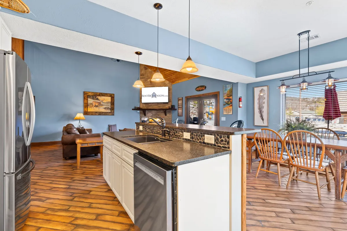 An expansive view of the open-concept kitchen, dining, and living area. The image showcases a central kitchen island, stainless steel appliances, a well-lit dining table, and a comfortable lounge space, all within an airy, sun-drenched setting.