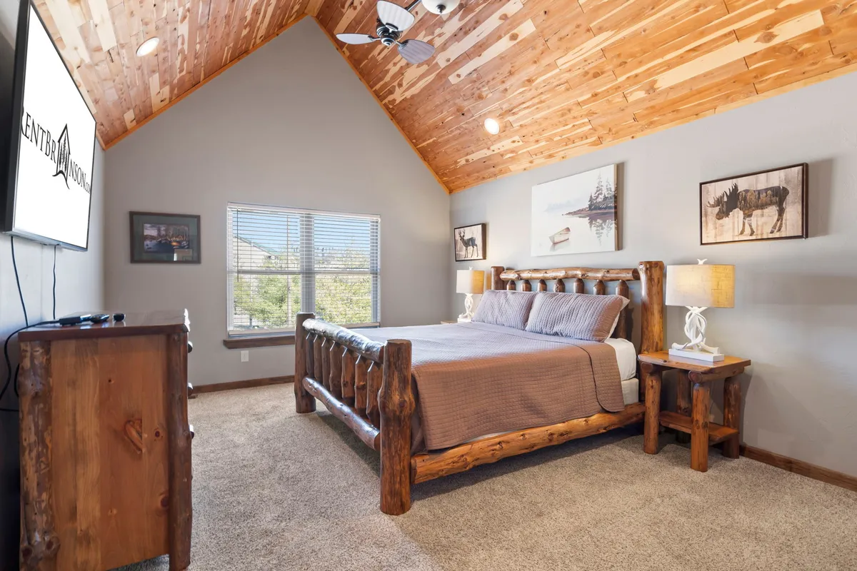 A tranquil bedroom featuring a log bed, wooden furniture, and simple artwork on the walls. A large window lets in natural light, and the overall mood is peaceful and rustic, ideal for relaxation or a good night’s sleep.