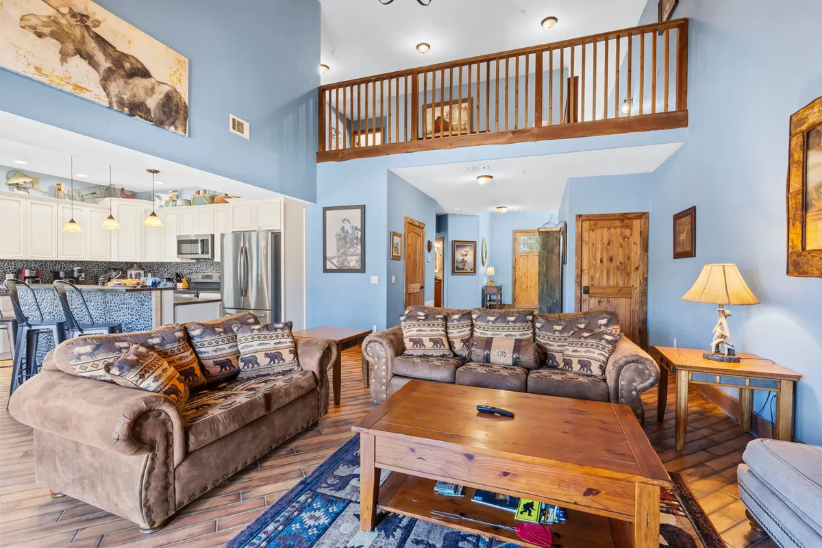 The image showcases a spacious and inviting living area with cozy sofas adorned with patterned cushions, a rustic wooden coffee table as the centerpiece, tasteful artwork on the walls, and a modern kitchen area in the background. The space is designed for comfort and togetherness, perfect for relaxing, entertaining, and sharing meals with family or friends.